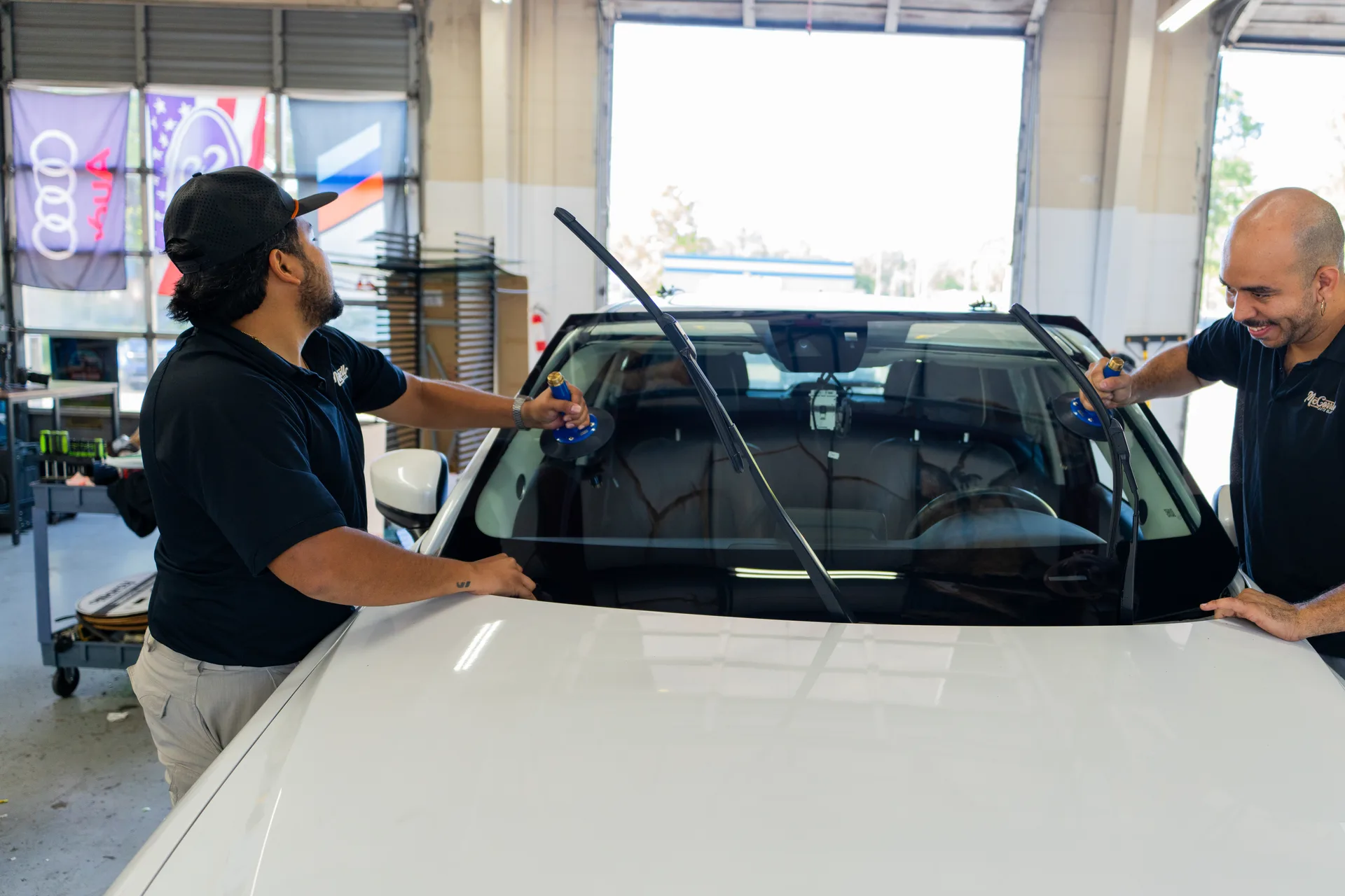 Two McConnell technicians positioning windshield glass on a white vehicle